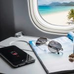 A smartphone with low battery held near an airplane window, showing a blurred aircraft wing in the background.